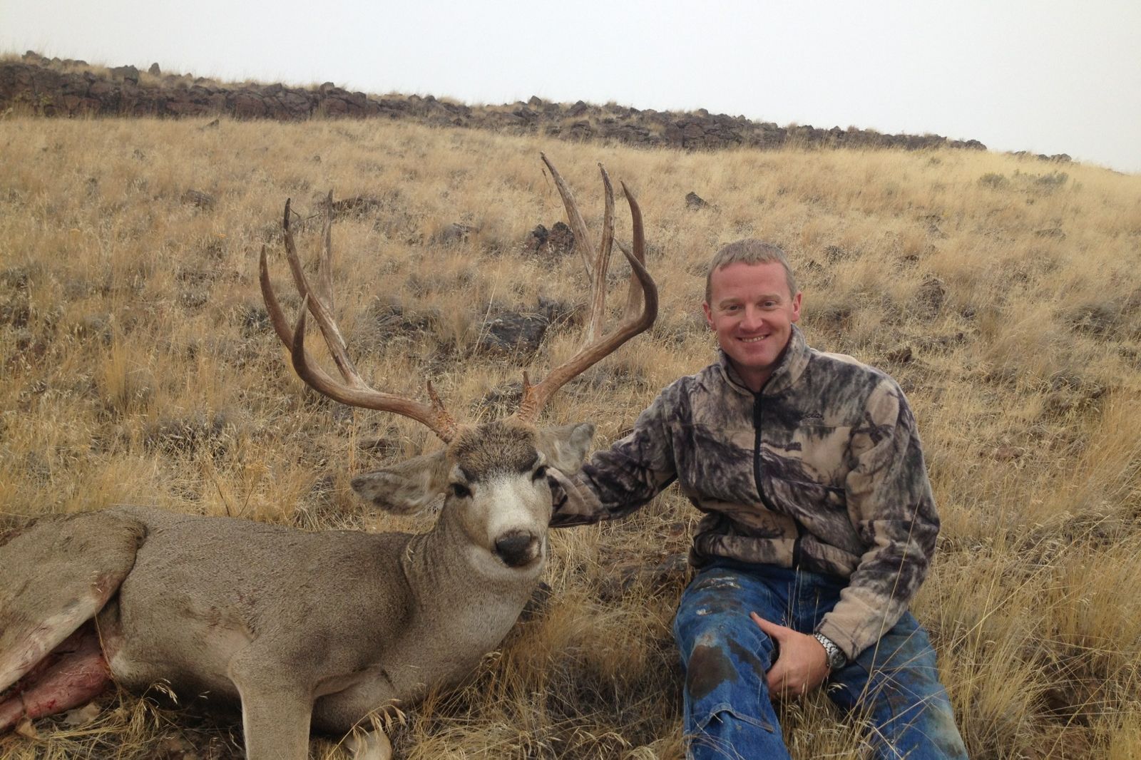 Hunter with a mule deer buck in dry grass
