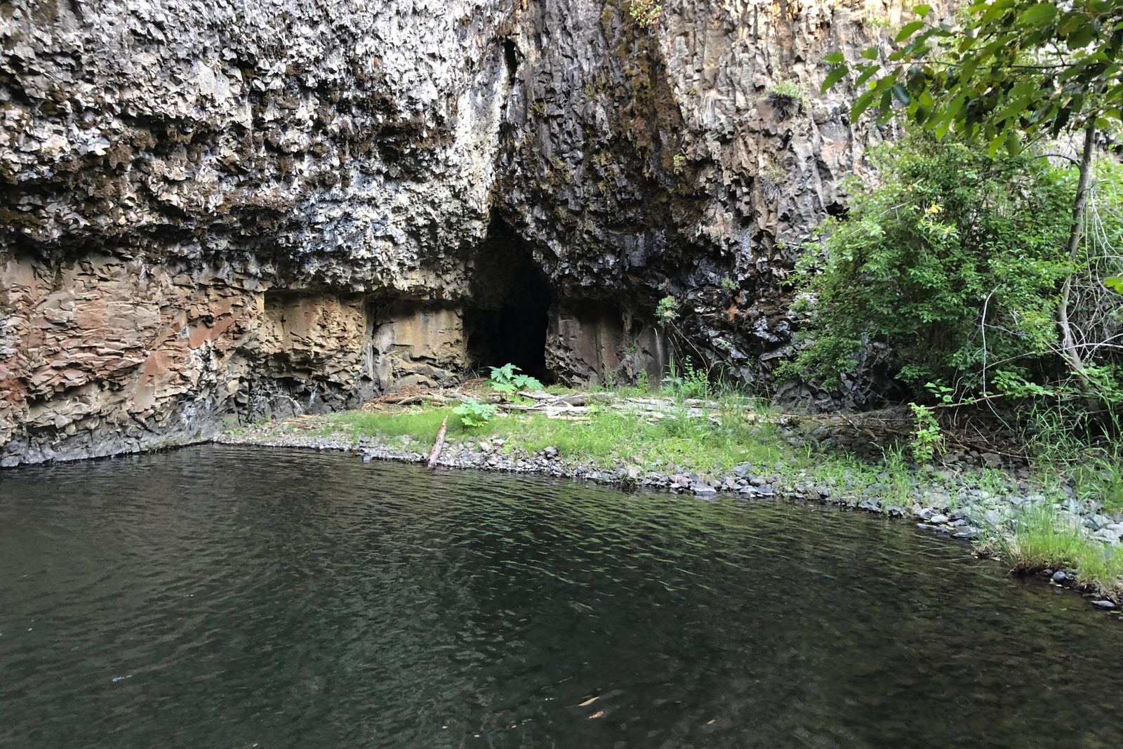 A cave in a basalt cliff above a quiet pool