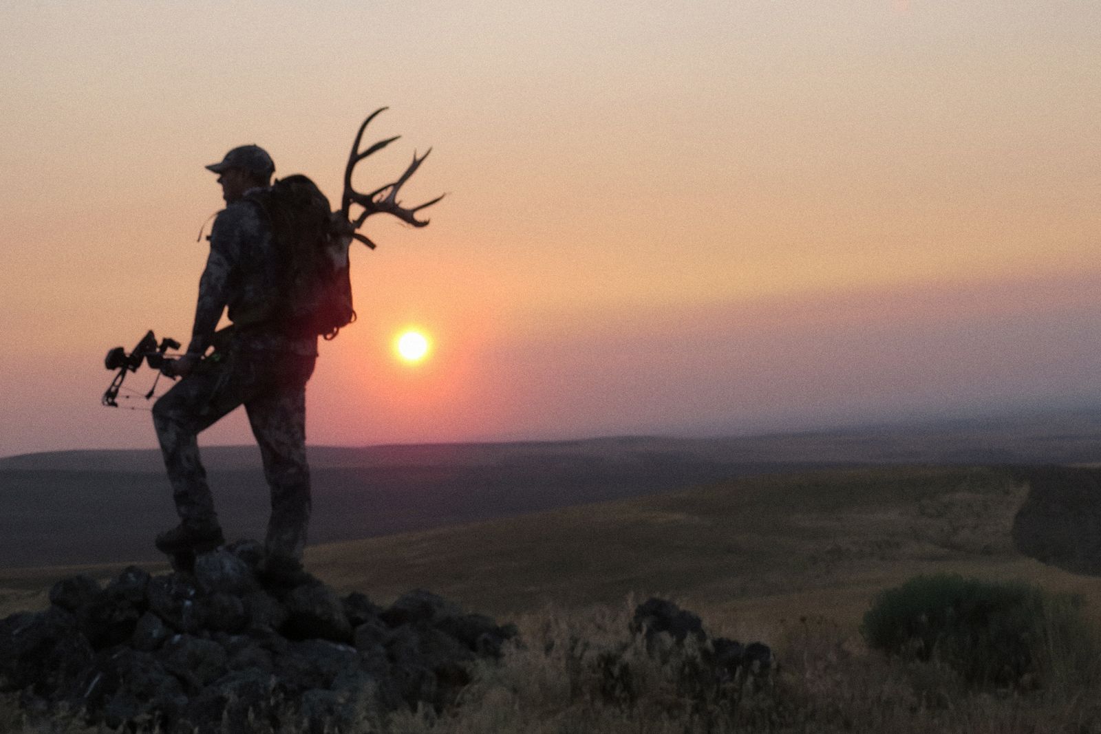 Bowhunter packing out antlers on the rimrock at sunset